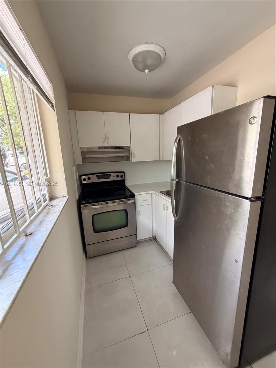 A small kitchen features white cabinets, stainless steel appliances, and light-colored tile flooring — 1194 NW 19th Ave # 1, Miami FL 33125, MIAMI, FL
