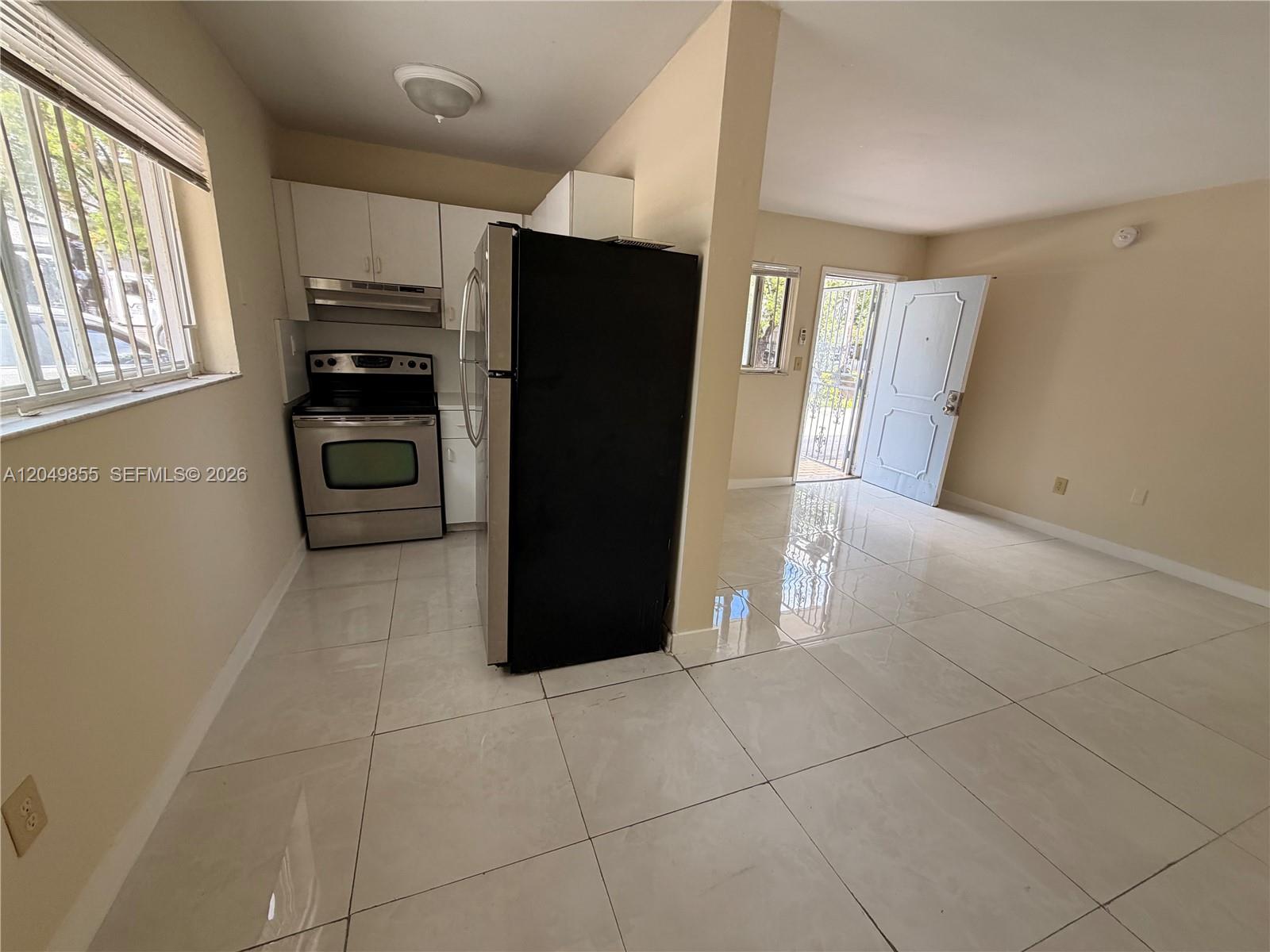 A kitchen with stainless steel appliances and white cabinets opens into a tiled living area — 1194 NW 19th Ave # 1, Miami FL 33125, MIAMI, FL