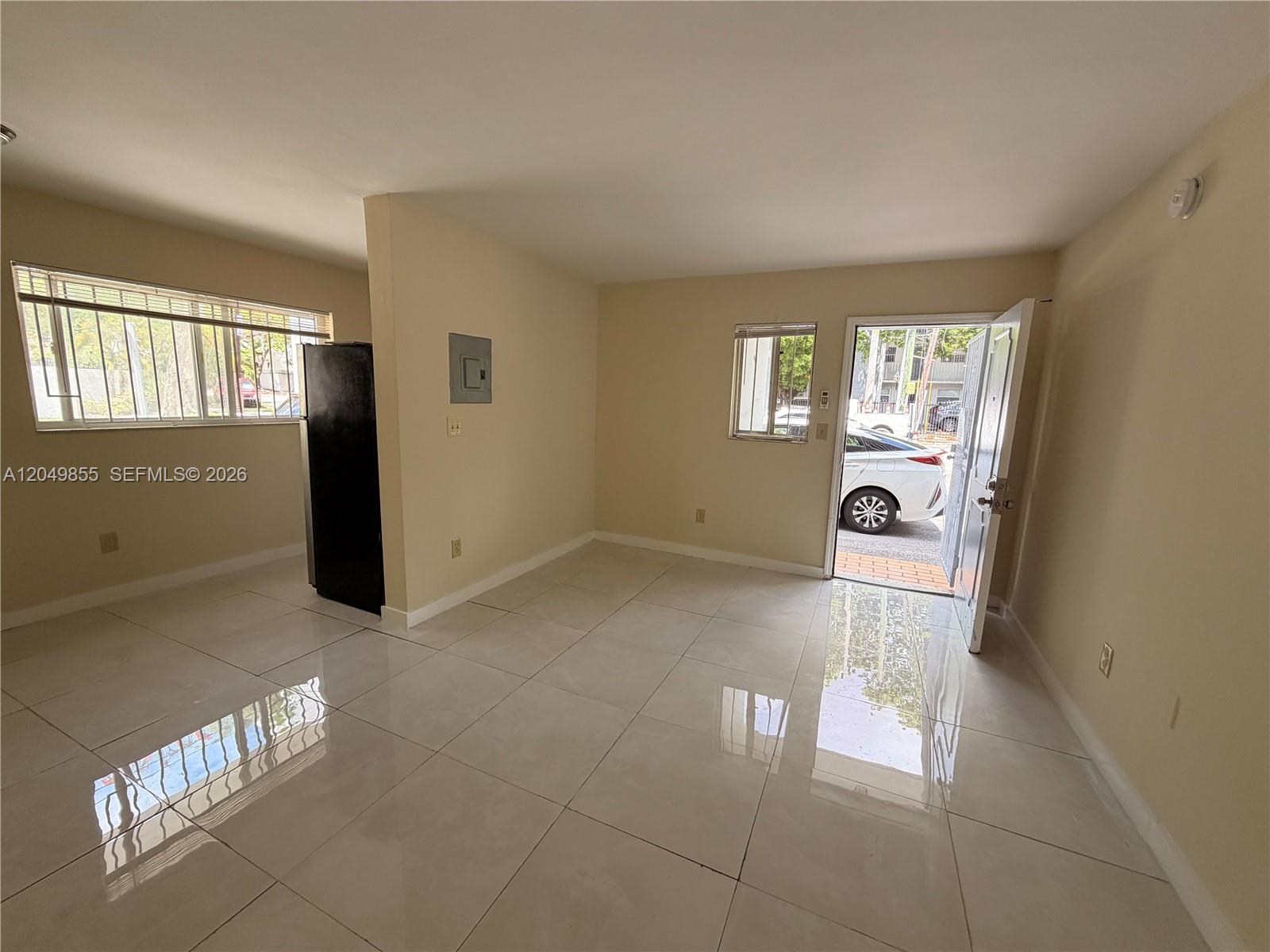 An interior view shows a room with light-colored tile flooring, a black refrigerator, and an open door — 1194 NW 19th Ave # 1, Miami FL 33125, MIAMI, FL