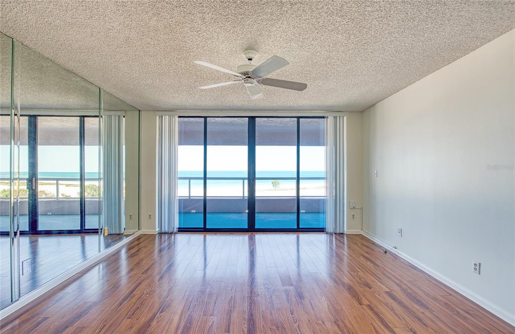 An empty room with wood flooring, mirrored walls, a ceiling fan, and sliding glass balcony doors — 1310 GULF BOULEVARD UNIT 4D, CLEARWATER BEACH, FL