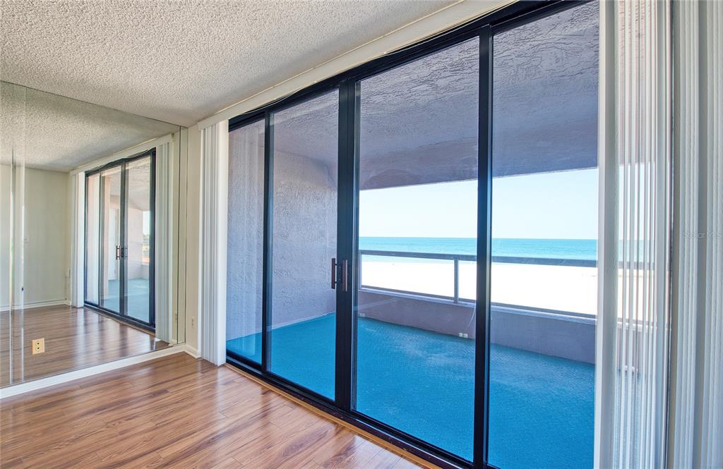 A room with wood-look flooring and a mirrored wall features sliding doors opening to a balcony — 1310 GULF BOULEVARD UNIT 4D, CLEARWATER BEACH, FL