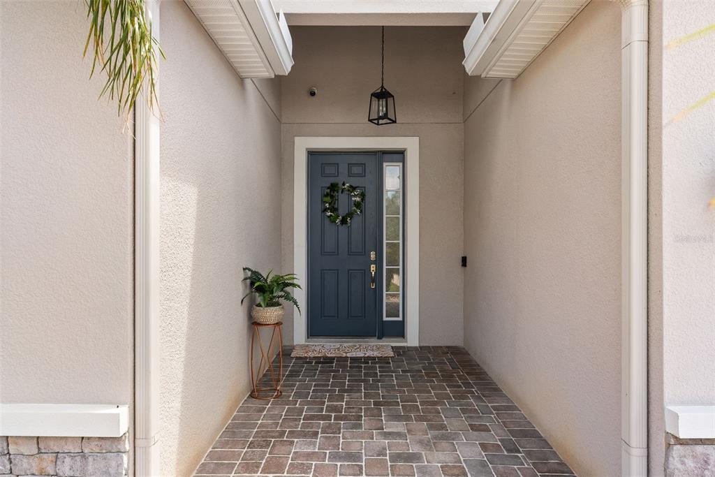 A covered entryway features a blue front door with a side window and brick pavers — 32373 BANNACK LANE, WESLEY CHAPEL, FL