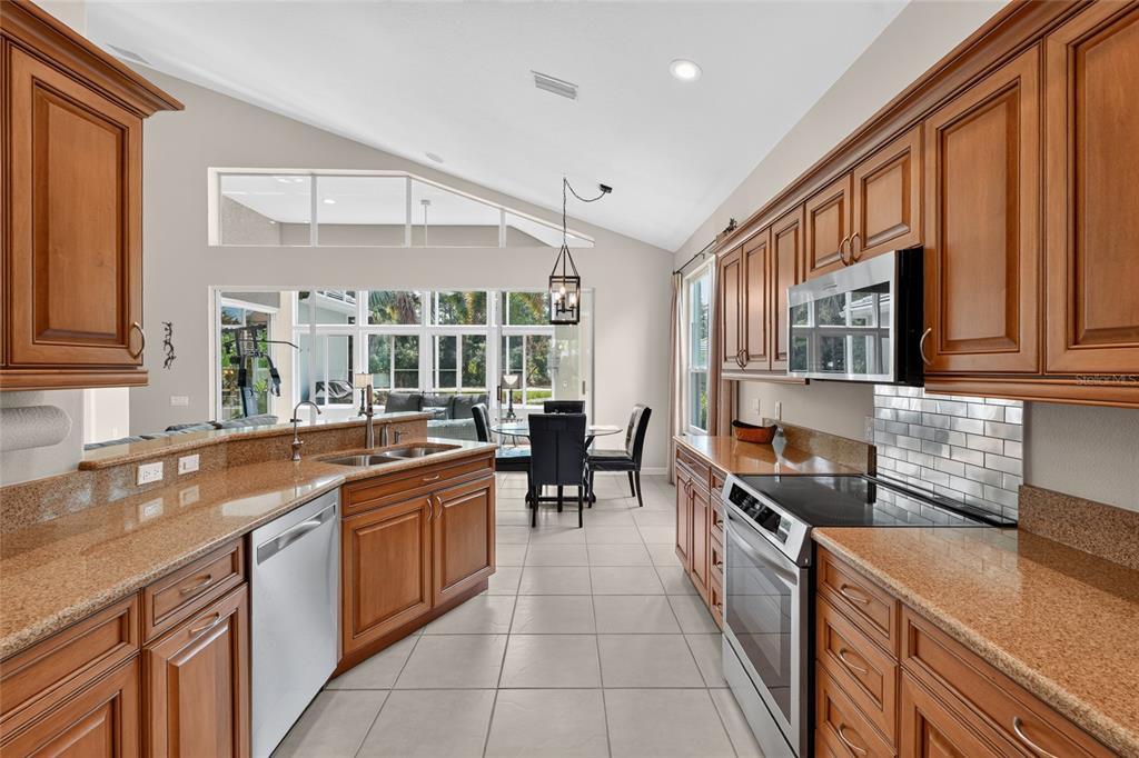 A kitchen with wood cabinets, granite countertops, and stainless steel appliances overlooks a dining area — 8415 WHISPERING WOODS COURT, BRADENTON, FL