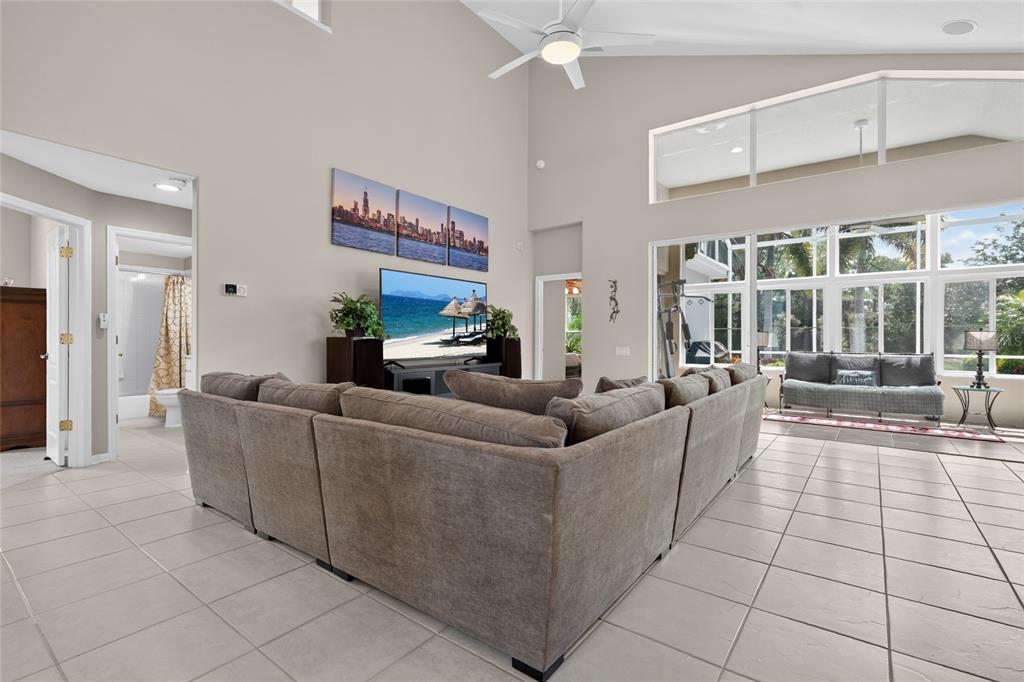 A spacious living room features a large sectional sofa, high ceilings, and floor-to-ceiling windows — 8415 WHISPERING WOODS COURT, BRADENTON, FL