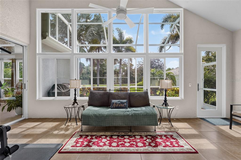 A sunroom features large windows, a daybed, a red area rug, and tile flooring — 8415 WHISPERING WOODS COURT, BRADENTON, FL