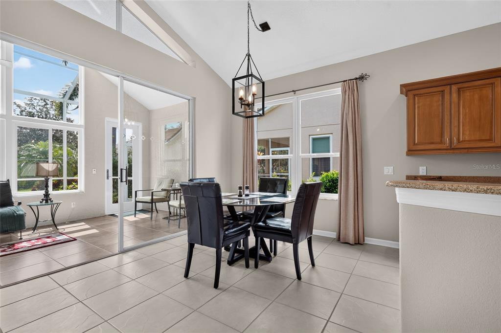 A dining area with a glass table, four chairs, and a view into a sunroom — 8415 WHISPERING WOODS COURT, BRADENTON, FL