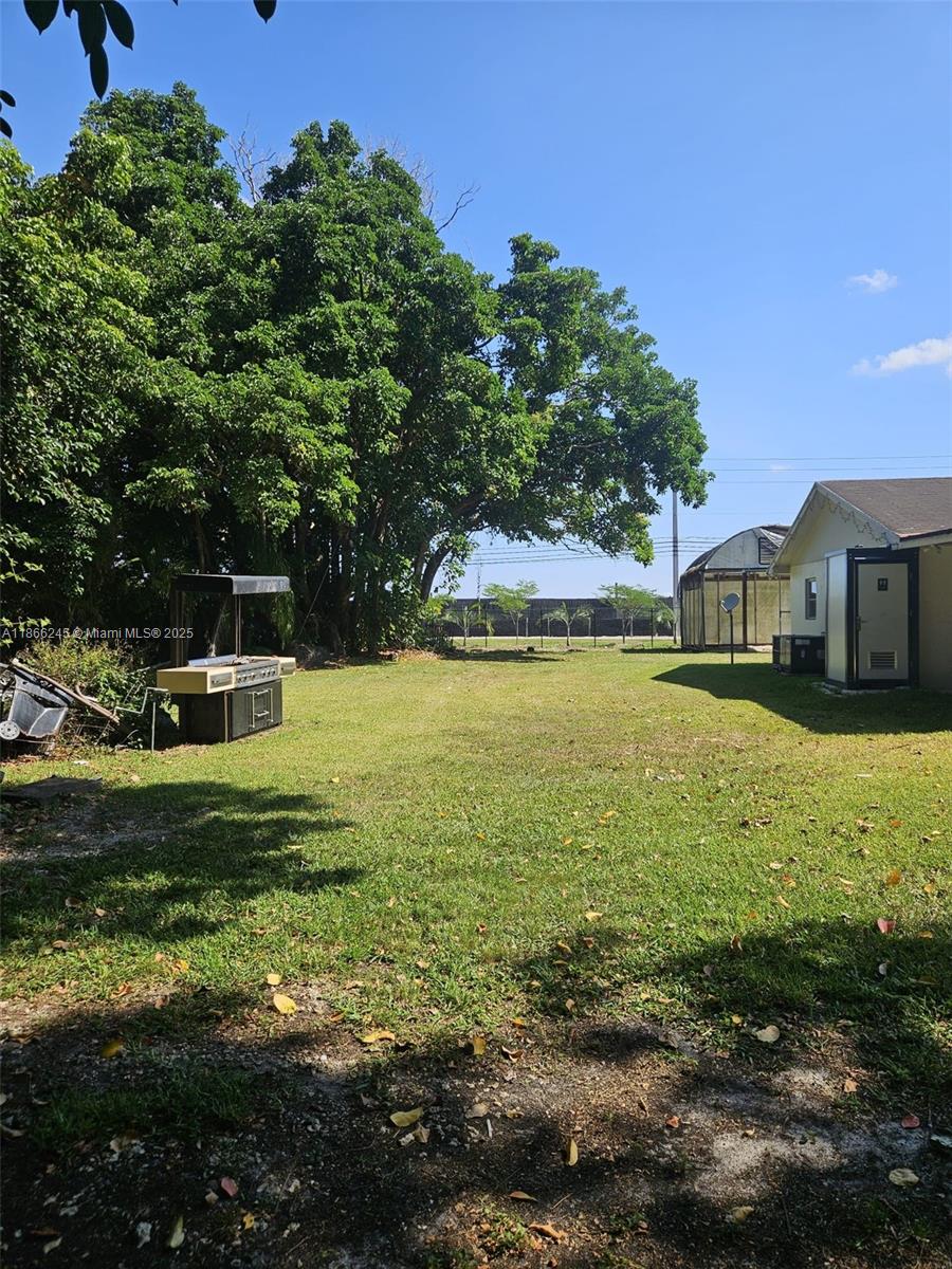 A grassy backyard features a large tree, a grill, and a small greenhouse structure — 19230 SW 216TH ST, Miami FL 33170, MIAMI, FL