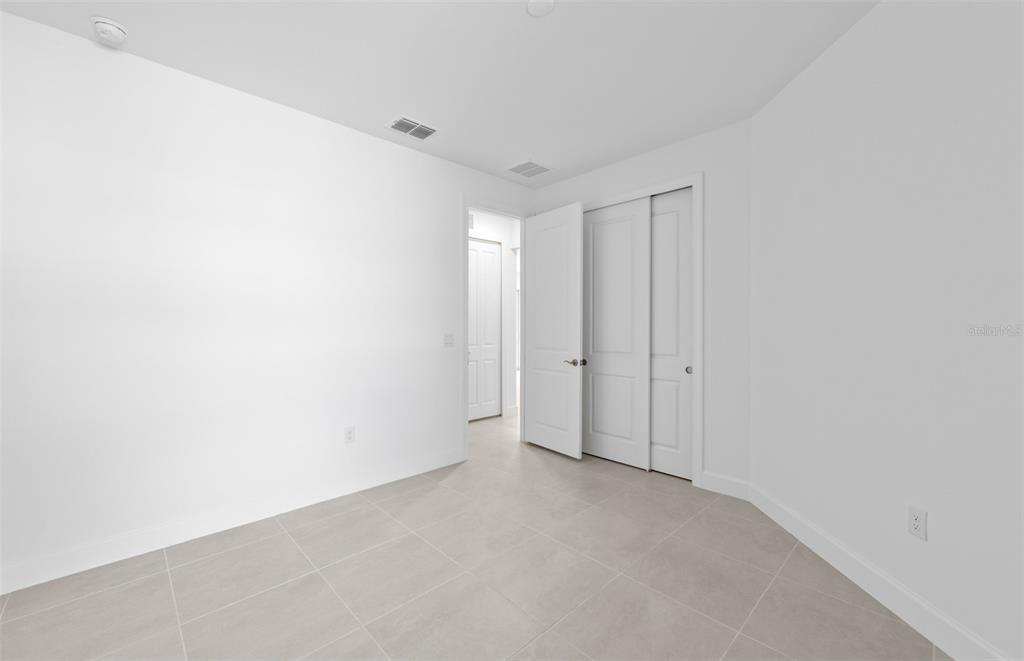 A bright, empty bedroom features white walls, tile flooring, and a sliding closet door — 27104 CLAM SHELL COURT, ENGLEWOOD, FL