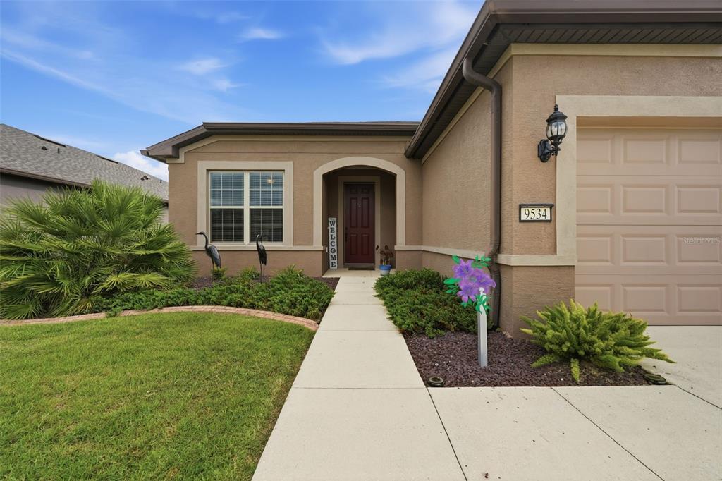 A beige single-story house features a dark front door, a concrete walkway, and landscaping — 9534 SW 65TH PLACE, OCALA, FL