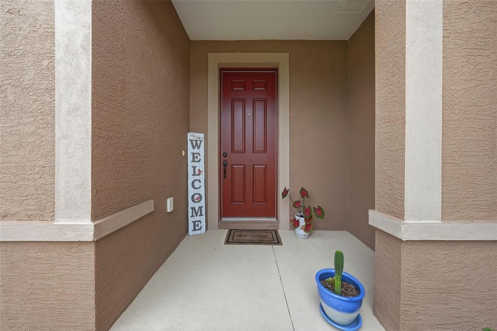 A red front door is centered on a covered porch with a cactus in a pot — 9534 SW 65TH PLACE, OCALA, FL