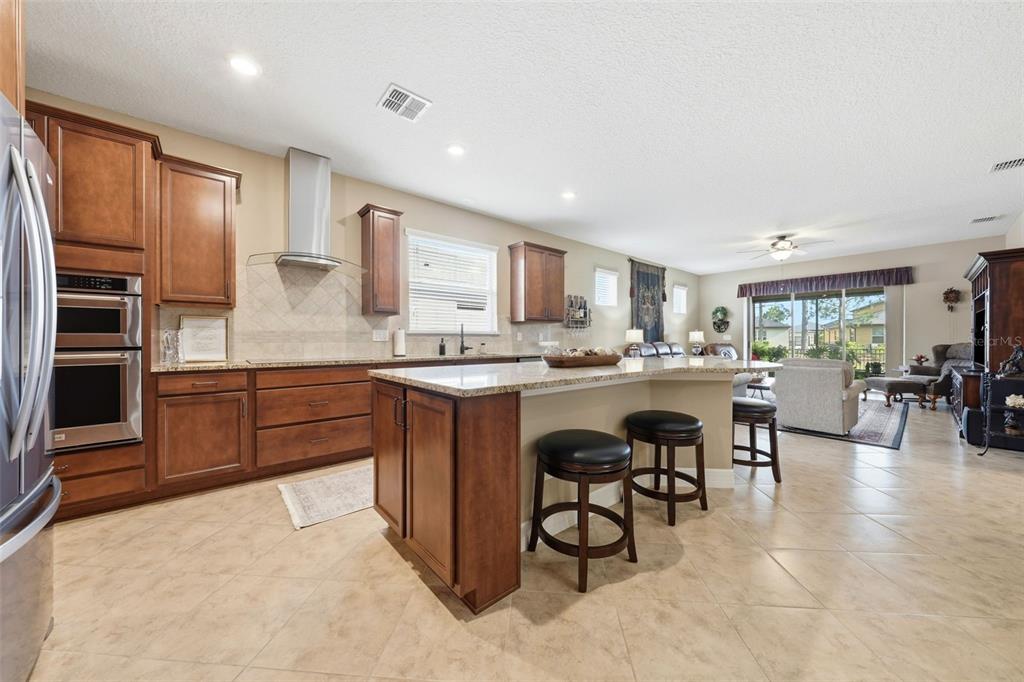 A kitchen with wood cabinets, granite countertops, and an island with bar stools — 9534 SW 65TH PLACE, OCALA, FL