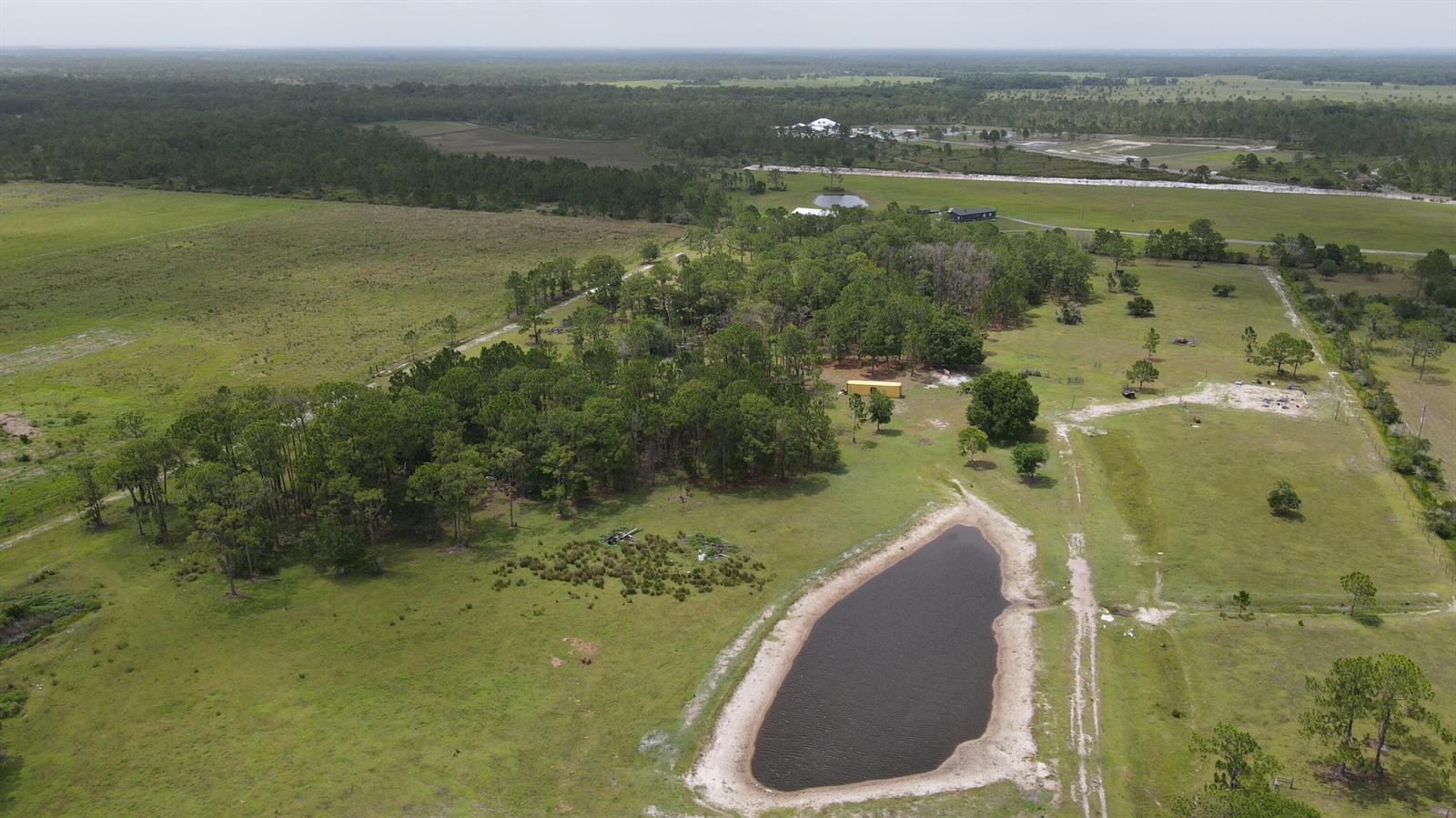An aerial view shows a rural property with a pond, trees, and open pasture land — 12271 NE 124th Avenue, Okeechobee FL 34972, OKEECHOBEE, FL