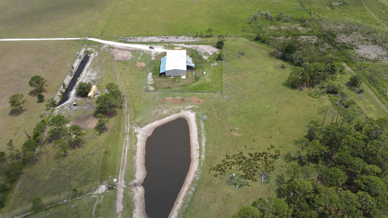 An aerial view shows a metal building, a pond, and a dirt road on pasture — 12271 NE 124th Avenue, Okeechobee FL 34972, OKEECHOBEE, FL