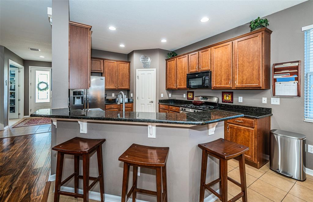 A kitchen features dark wood cabinets, granite countertops, a breakfast bar with stools, and tile flooring — 3515 ALBRITTON STREET, NEW PORT RICHEY, FL