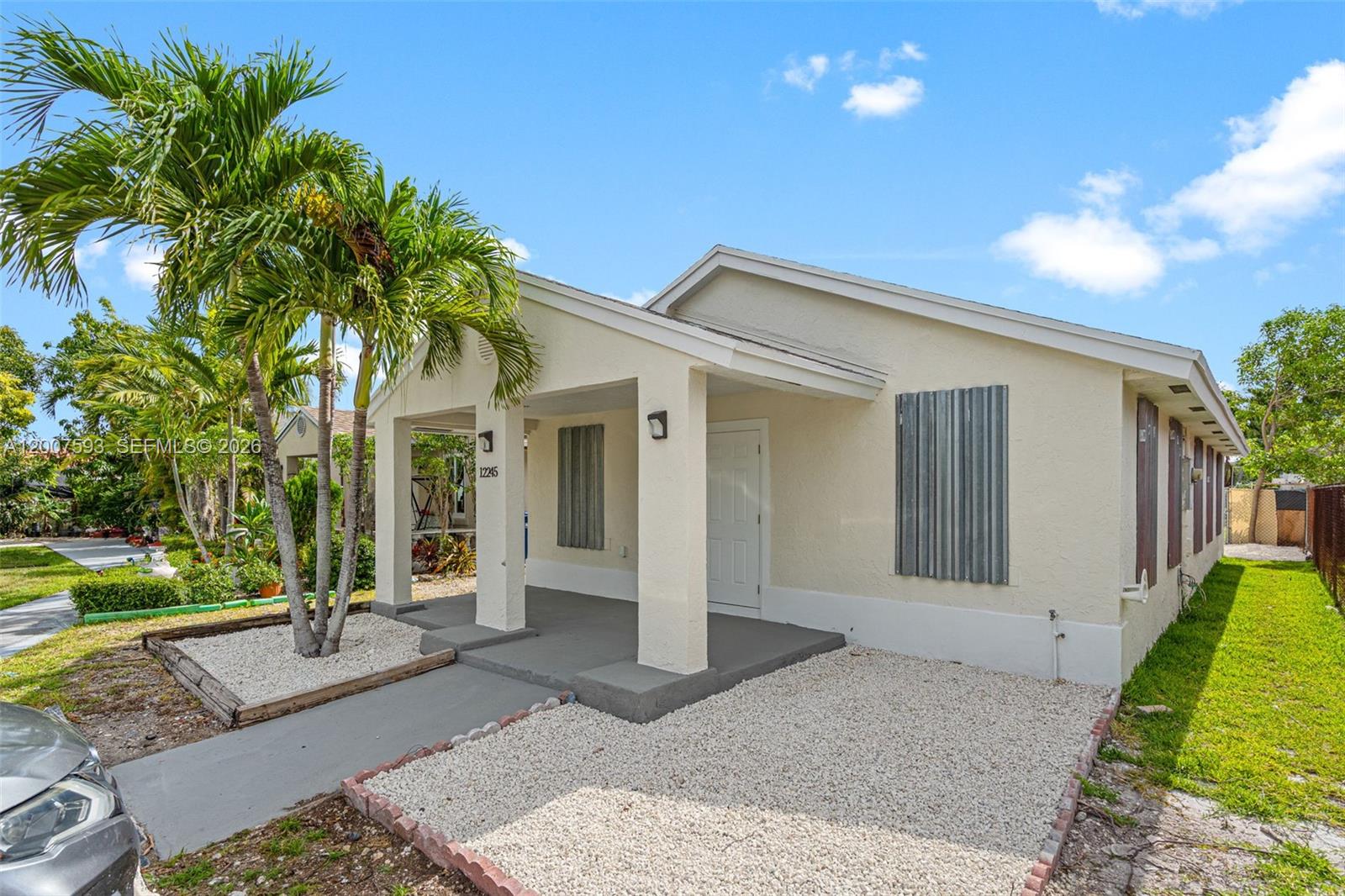 A single-story house features a covered front porch, gravel landscaping, and metal hurricane shutters — 12245 SW 201st Ter, Miami FL 33177, MIAMI, FL