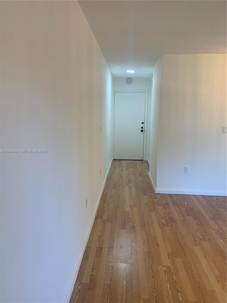A hallway with light-colored walls and wood-look flooring leads to a white door — 2460 SW 18th Ave # 1205, Miami FL 33145, MIAMI, FL