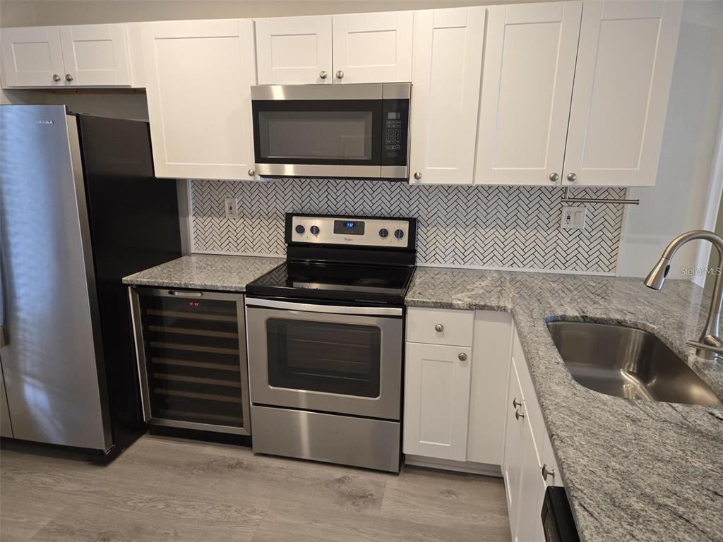 A kitchen features white cabinets, stainless steel appliances, granite countertops, and a herringbone tile backsplash — 6218 PALMA DEL MAR BOULEVARD S UNIT 213, ST PETERSBURG, FL