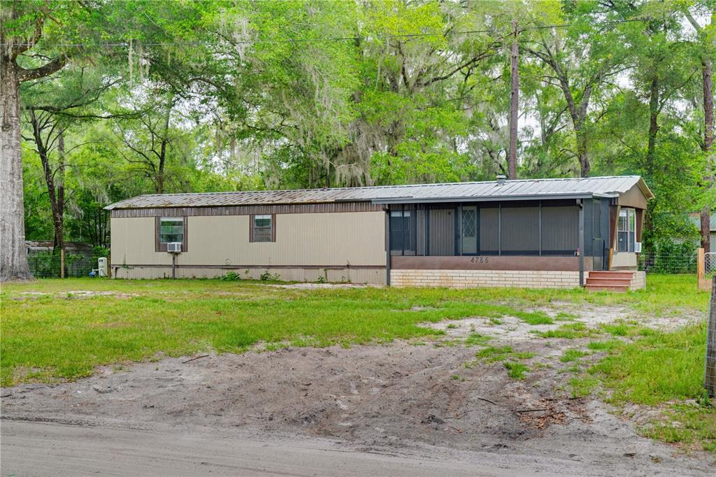 A single-story mobile home with a screened-in porch sits on a grassy lot with trees — 4786 SW 122ND LANE, WEBSTER, FL