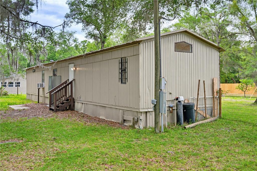 The exterior of a beige mobile home features metal siding, a wooden staircase, and trees — 4786 SW 122ND LANE, WEBSTER, FL