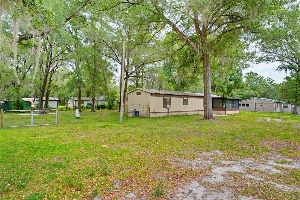 A tan mobile home sits on a grassy lot surrounded by large, moss-draped trees — 4786 SW 122ND LANE, WEBSTER, FL