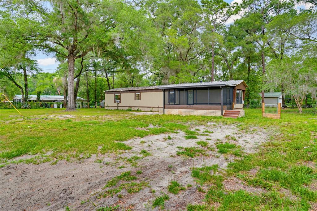 A single-story mobile home with a screened-in porch sits on a large, grassy lot — 4786 SW 122ND LANE, WEBSTER, FL