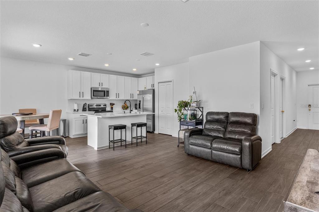 An open-concept kitchen and living area features white cabinetry, a kitchen island, and dark flooring — 4120 TUG HILL LANE, DELTONA, FL