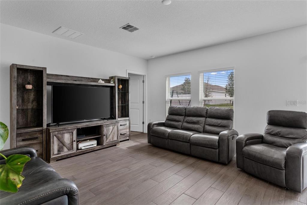 A living room features dark wood-look tile flooring, a gray entertainment center, and leather furniture — 4120 TUG HILL LANE, DELTONA, FL