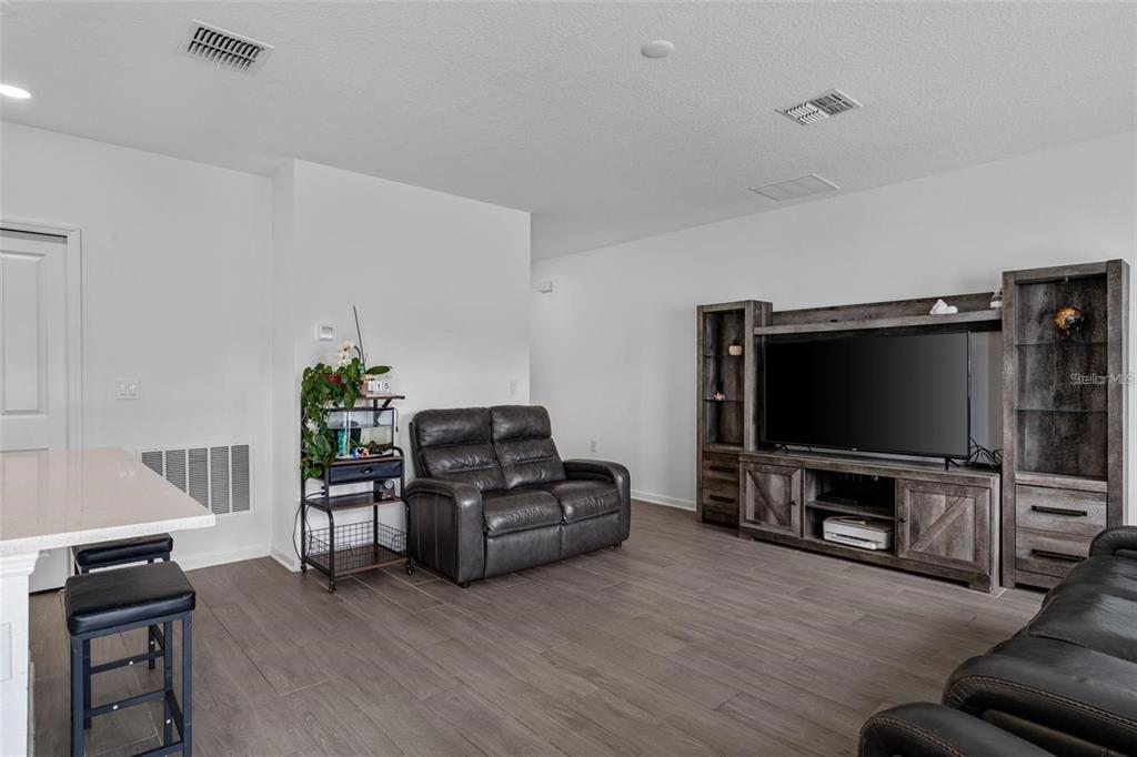 A living room features wood-look flooring, a dark leather loveseat, and a large entertainment center — 4120 TUG HILL LANE, DELTONA, FL