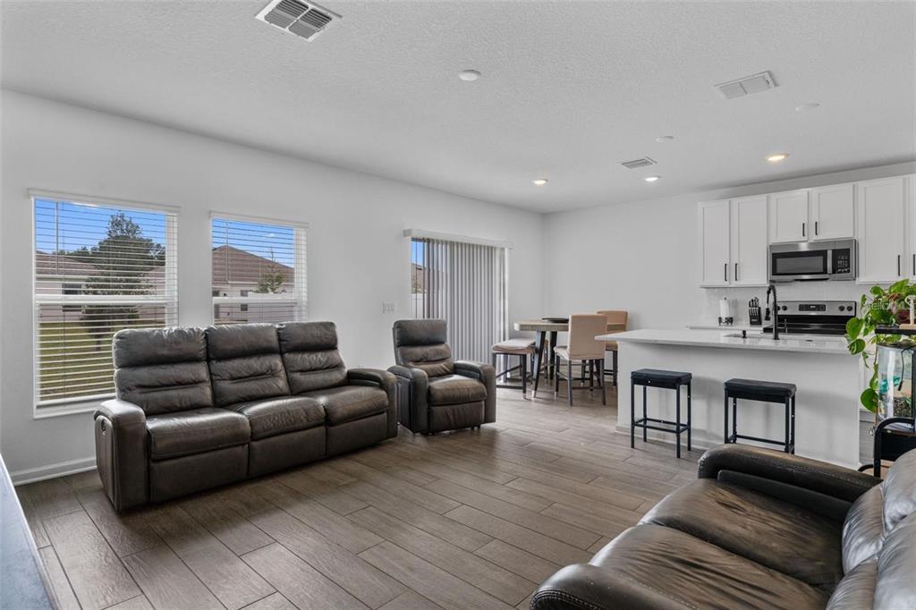 An open-concept living room and kitchen featuring dark leather furniture, tile flooring, and white cabinets — 4120 TUG HILL LANE, DELTONA, FL
