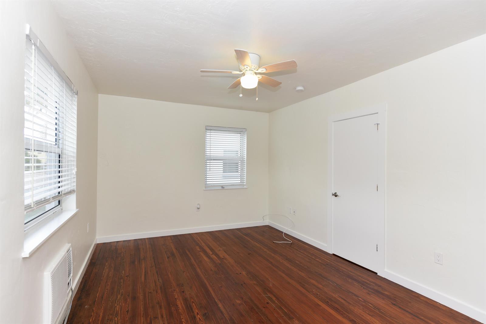 An empty bedroom features white walls, dark wood flooring, a ceiling fan, and two windows — 717 2nd Ave # 5, FL 33460, FL