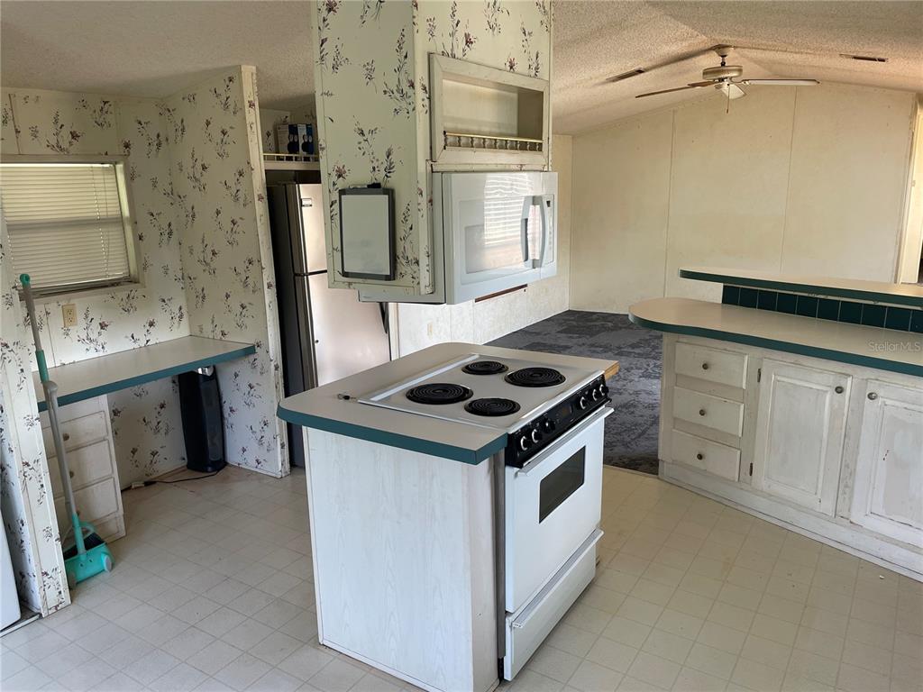 A kitchen features white cabinets, a floral wallpapered wall, and a central stove island — 8929 HONEYWELL ROAD, GIBSONTON, FL