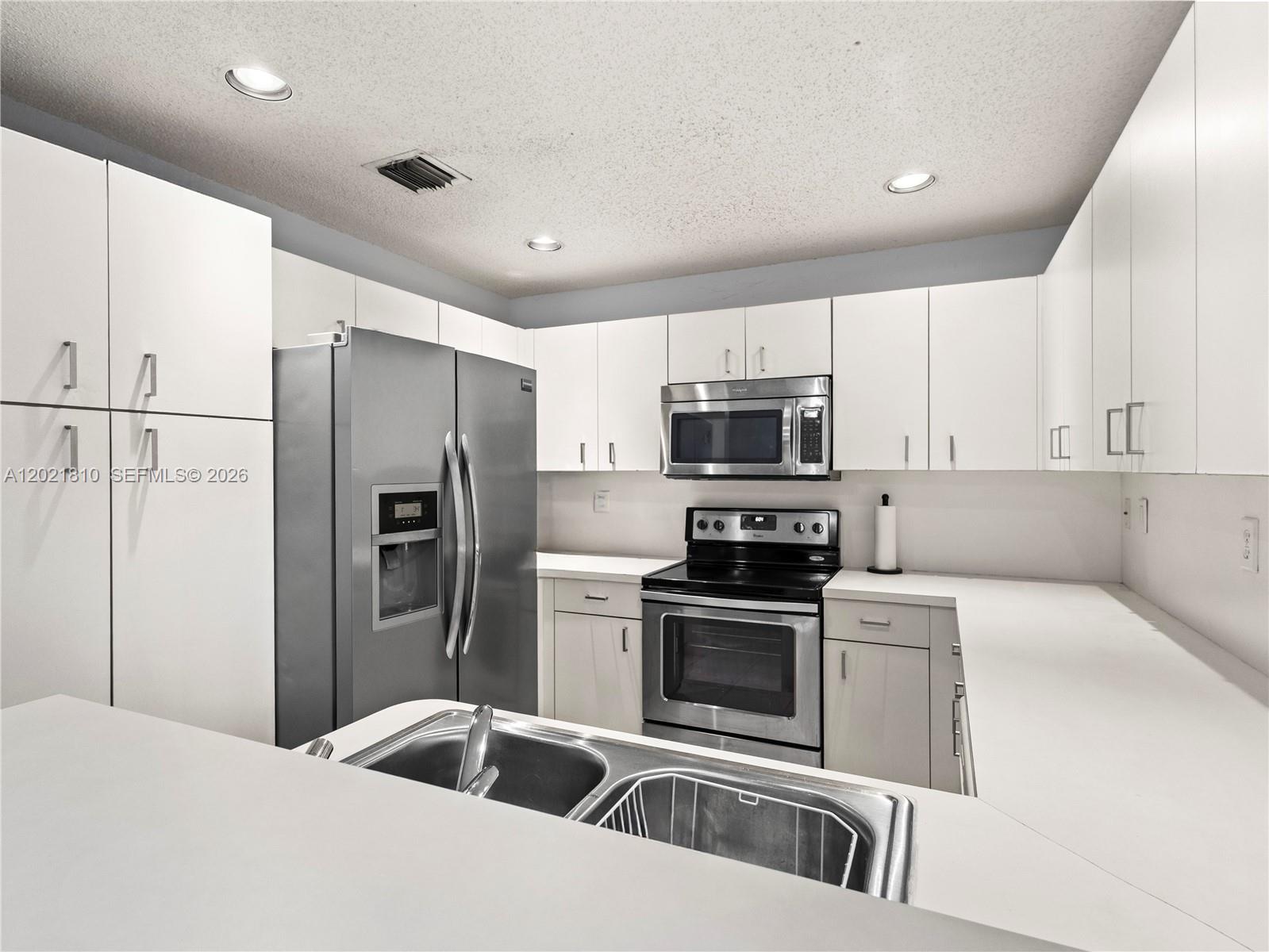 A kitchen features white cabinets, stainless steel appliances, and a double-basin sink on white countertops — 5033 NW 114th Ct, Doral FL 33178, DORAL, FL