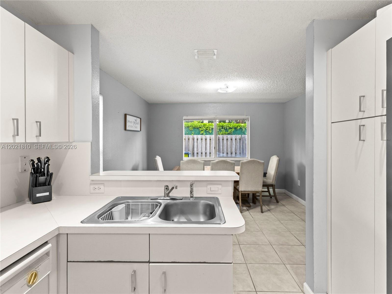 A kitchen with white cabinets and a stainless steel sink overlooks a dining area — 5033 NW 114th Ct, Doral FL 33178, DORAL, FL
