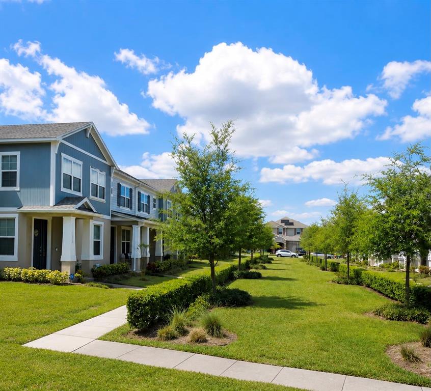 A row of blue townhouses sits beside a grassy lawn with trees and a sidewalk — 12042 GRANDROSE ALLEY, WINTER GARDEN, FL
