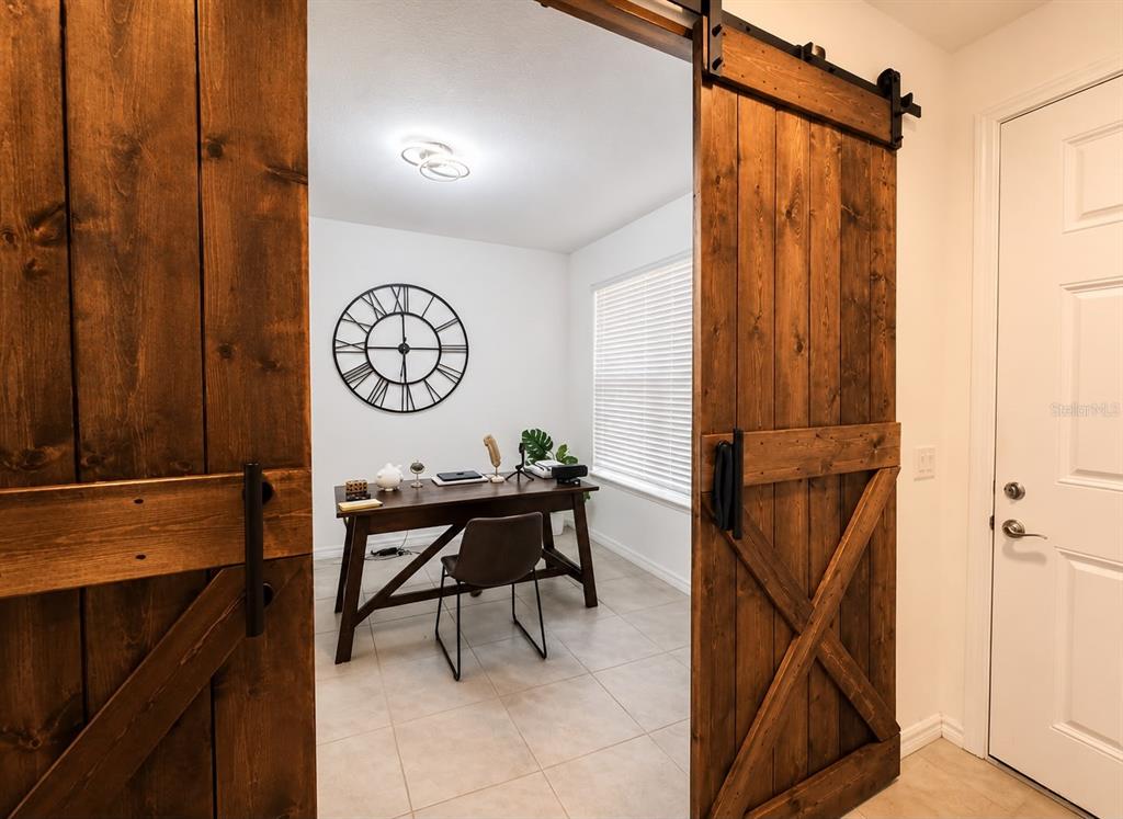 A home office with a wooden desk and chair is visible through large sliding barn doors — 12042 GRANDROSE ALLEY, WINTER GARDEN, FL