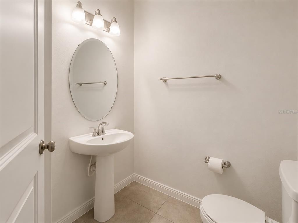 A small bathroom features a pedestal sink, oval mirror, wall-mounted towel bar, and toilet — 12042 GRANDROSE ALLEY, WINTER GARDEN, FL