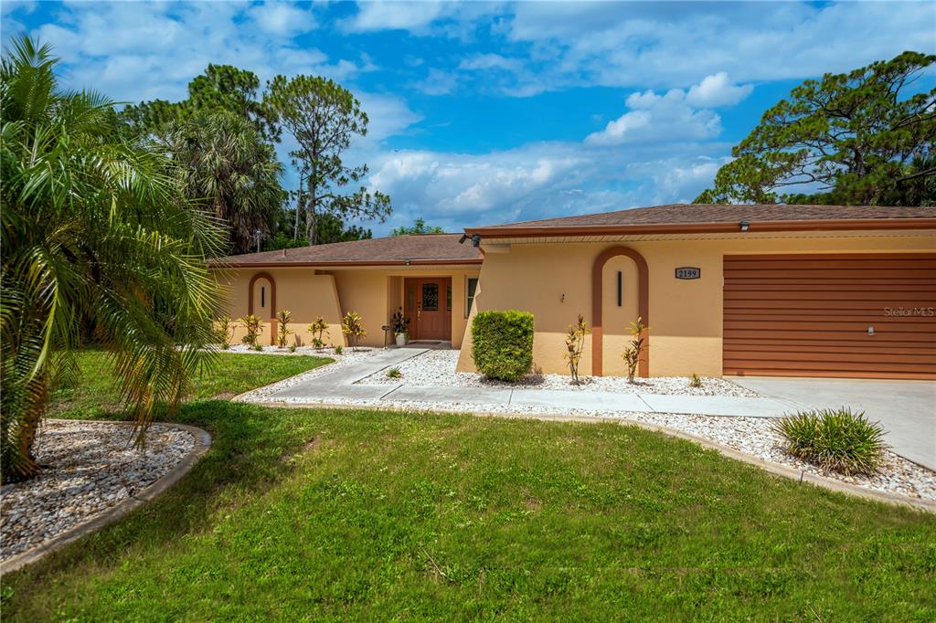 A single-story house with a yellow stucco exterior, a two-car garage, and a sunset sky — 2199 BENDWAY DRIVE, PORT CHARLOTTE, FL