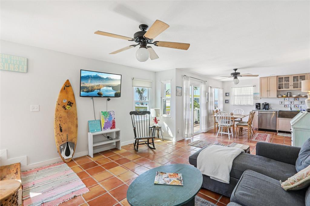 An open-concept living and dining area features terracotta tile floors, a surfboard, and kitchen — 23 80TH AVENUE, TREASURE ISLAND, FL