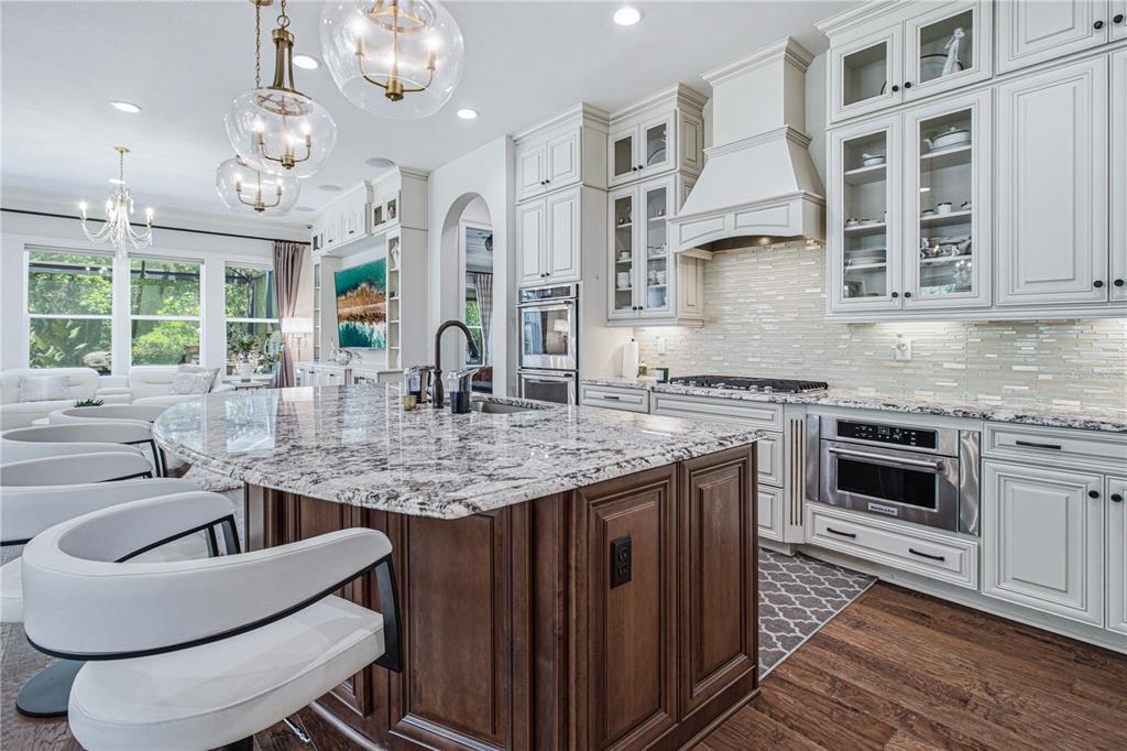 A kitchen features a large granite-topped island, white cabinetry, stainless steel appliances, and wood flooring — 3169 PARADOR WAY, JACKSONVILLE, FL