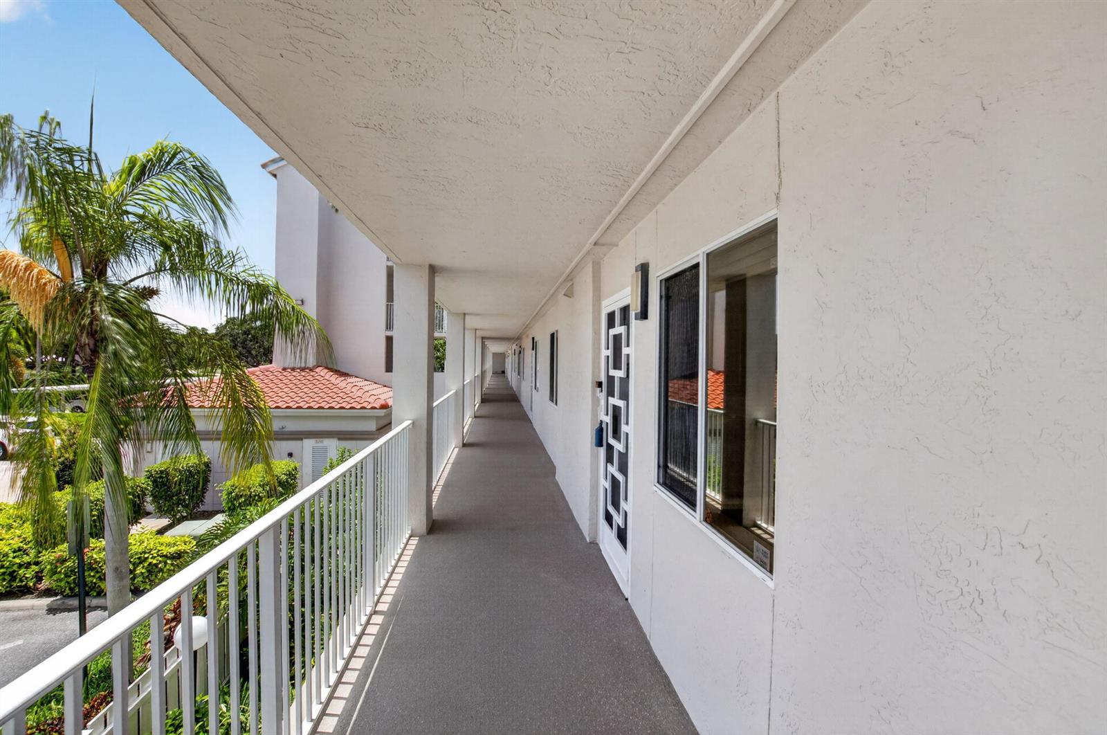 An outdoor apartment building walkway with white railings, stucco walls, and a concrete floor — 14111 Royal Vista Drive # 207, Delray Beach FL 33484, DELRAY BEACH, FL