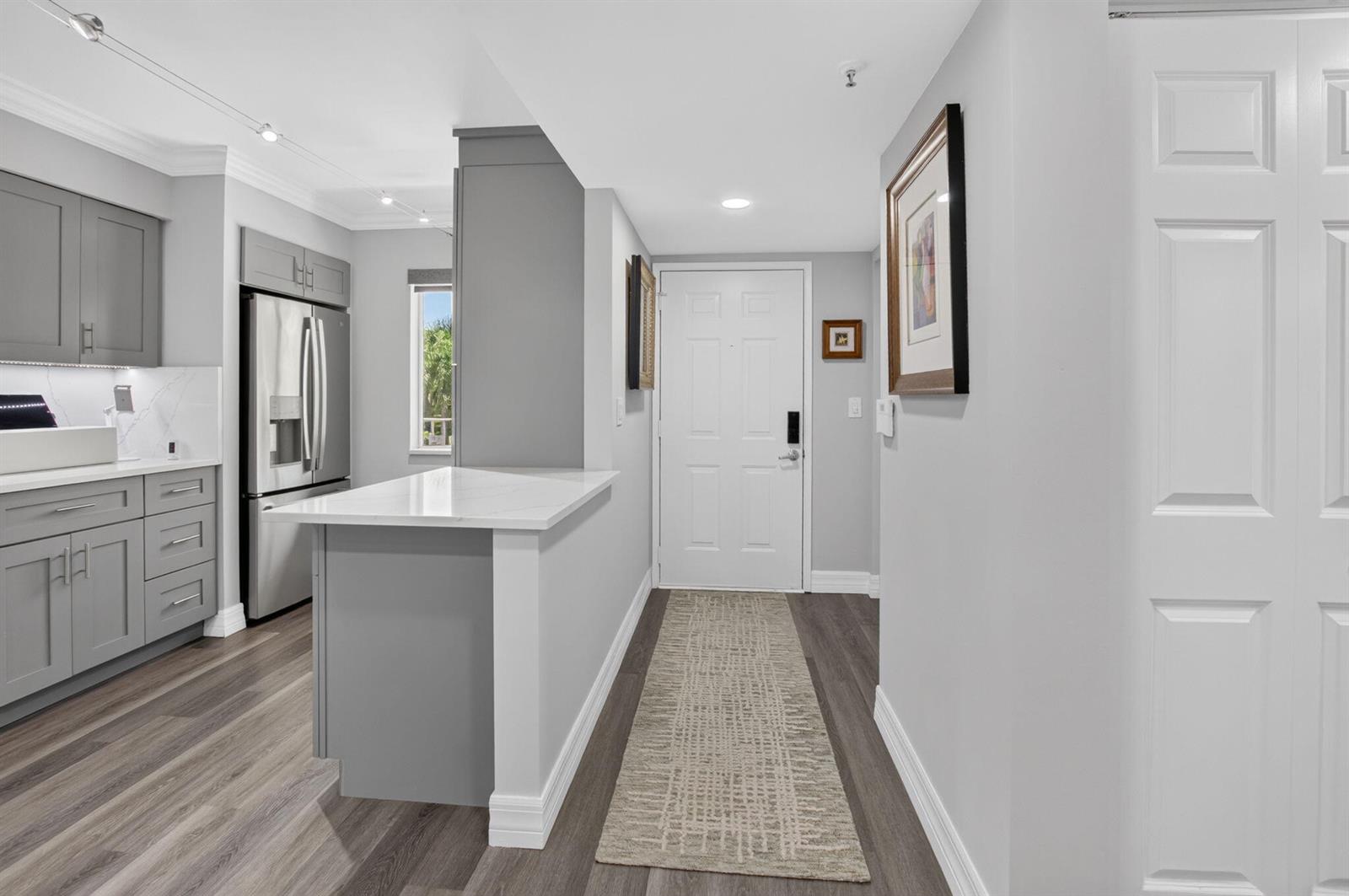 A kitchen with gray cabinets and a white countertop opens into an entryway with flooring — 14111 Royal Vista Drive # 207, Delray Beach FL 33484, DELRAY BEACH, FL