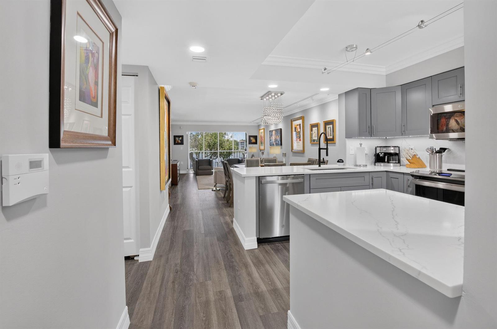 A modern kitchen with grey cabinets and white countertops opens into a living area — 14111 Royal Vista Drive # 207, Delray Beach FL 33484, DELRAY BEACH, FL