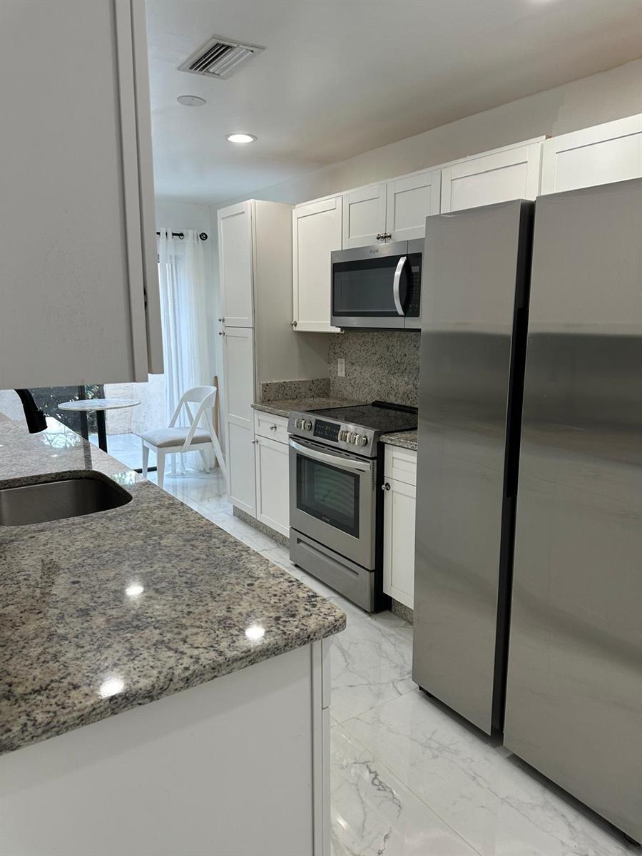 A kitchen features white cabinets, granite countertops, stainless steel appliances, and white marble-look flooring — 21866 Cypress Circle # 31c, Boca Raton FL 33433, BOCA RATON, FL