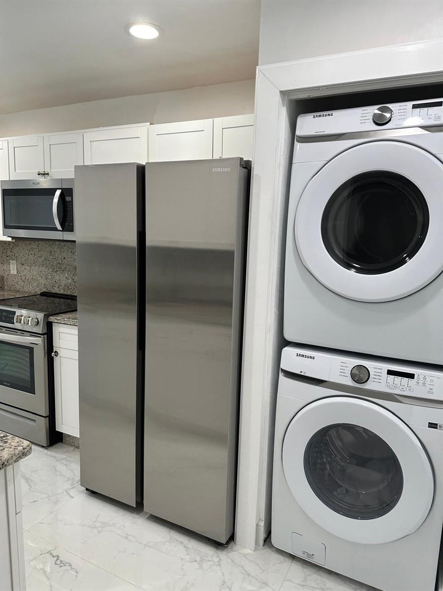 A kitchen features stainless steel appliances, white cabinetry, and a stacked Samsung washer and dryer — 21866 Cypress Circle # 31c, Boca Raton FL 33433, BOCA RATON, FL
