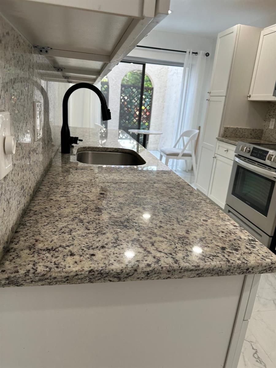 A kitchen features granite countertops, a black faucet, white cabinets, and a view of a patio — 21866 Cypress Circle # 31c, Boca Raton FL 33433, BOCA RATON, FL