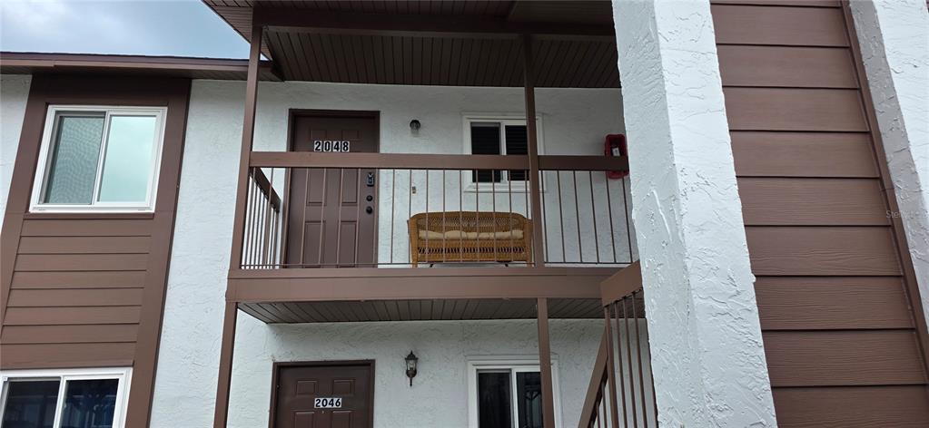 The exterior view shows a two-story apartment building with brown doors, balconies, and white siding — 39132 COUNTY ROAD 54 UNIT 2048, ZEPHYRHILLS, FL