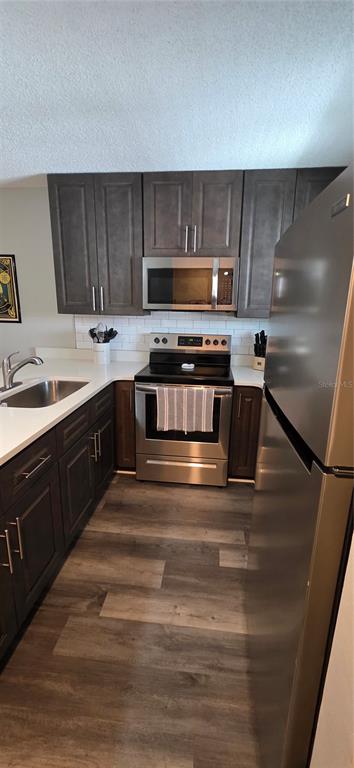 A kitchen features dark wood cabinets, stainless steel appliances, white countertops, and wood-look flooring — 39132 COUNTY ROAD 54 UNIT 2048, ZEPHYRHILLS, FL