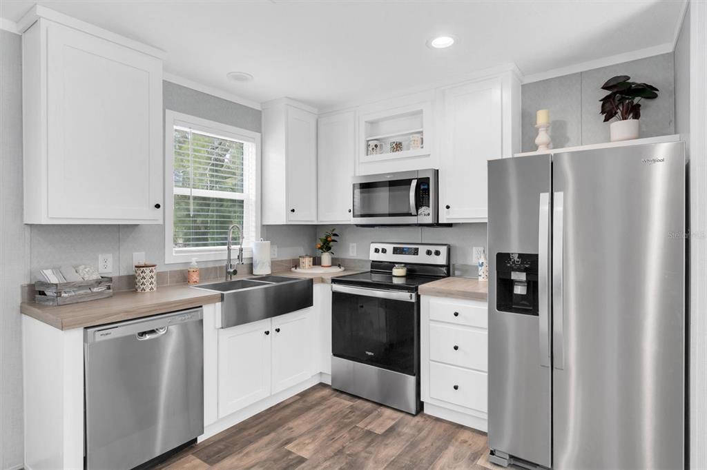 A kitchen features white cabinets, stainless steel appliances, a farmhouse sink, and wood-look flooring — 10617 DENTON AVENUE, HUDSON, FL