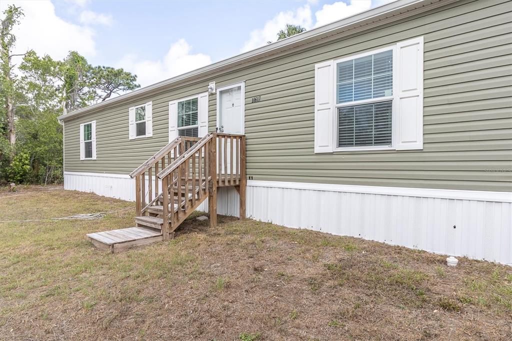 A light green manufactured home features white trim, a wooden staircase, and a white door — 10617 DENTON AVENUE, HUDSON, FL