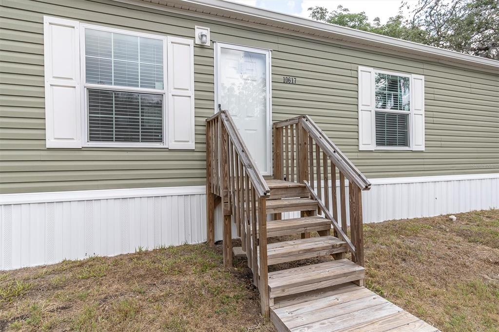 A light green mobile home exterior features a wooden staircase leading to the front door — 10617 DENTON AVENUE, HUDSON, FL